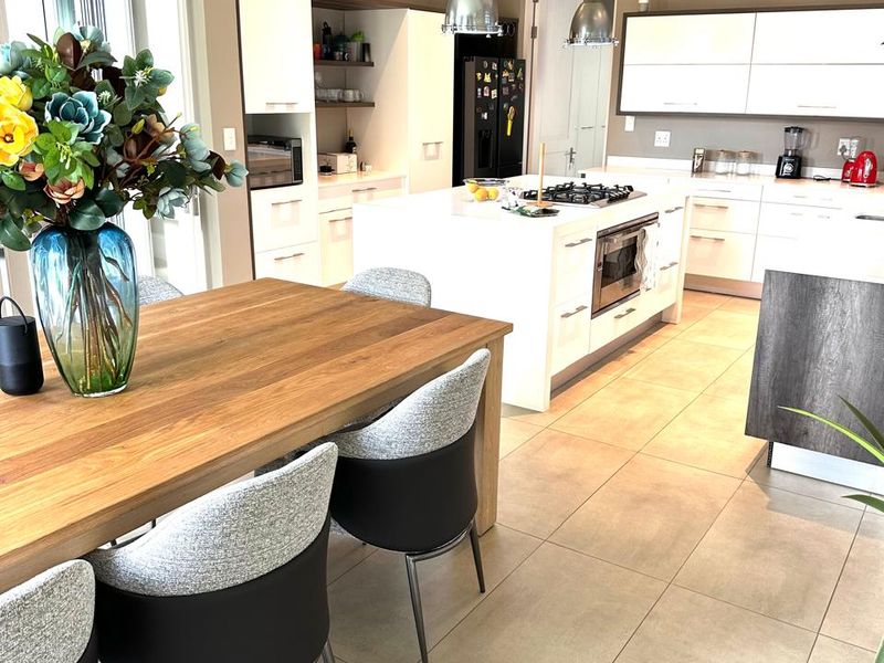Modern open-plan kitchen and dining area featuring a central island with gas hob, sleek cabinetry, tiled floors, and contemporary pendant lighting.
