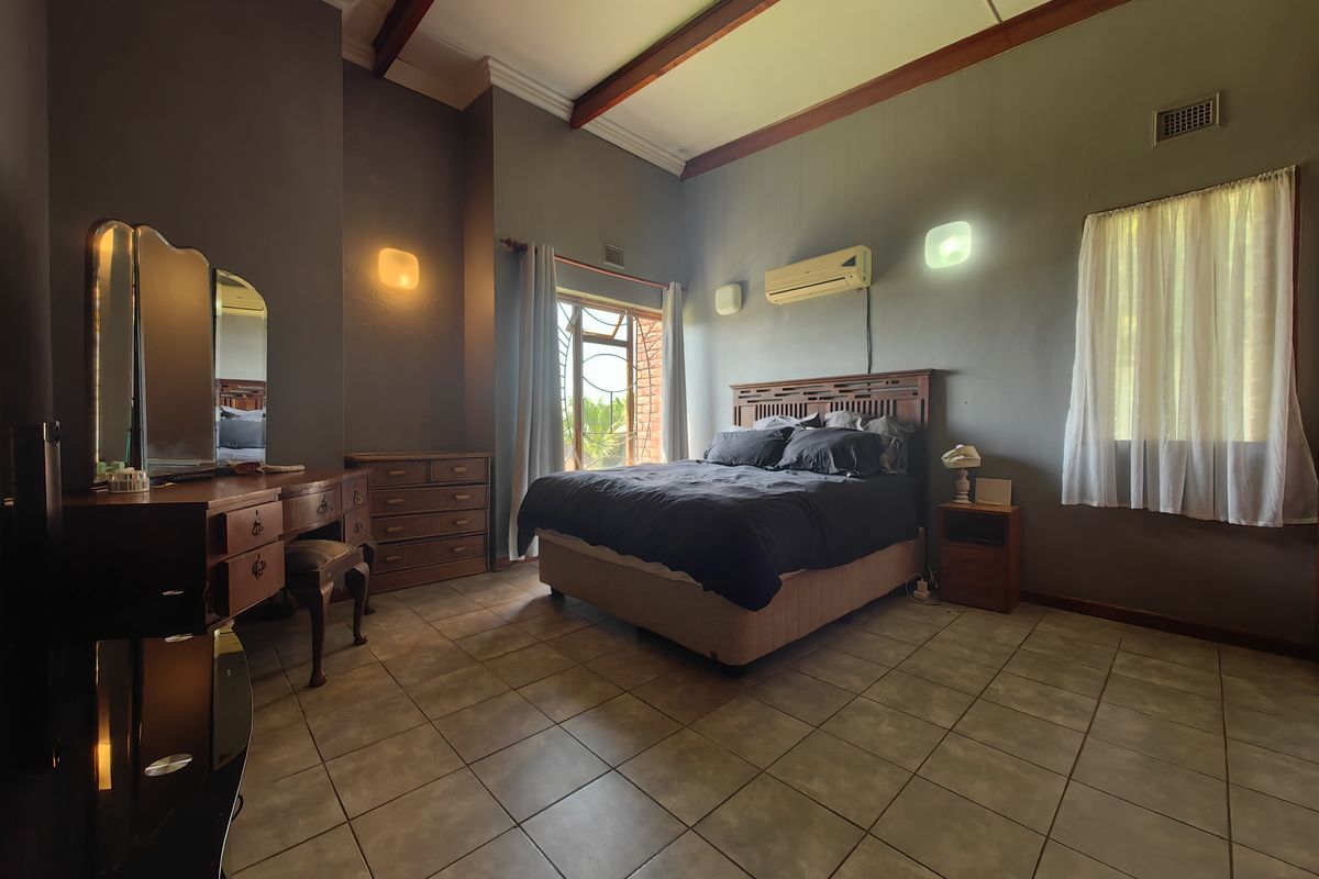 Spacious bedroom featuring tiled flooring, exposed timber ceiling beams, and a wall-mounted air conditioning unit, offering a comfortable and functional living space.