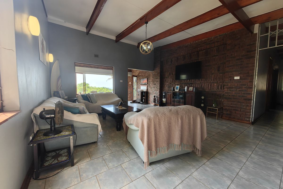 Spacious living room featuring exposed timber ceiling beams, a rustic brick feature wall, and neutral ceramic floor tiles with natural light.