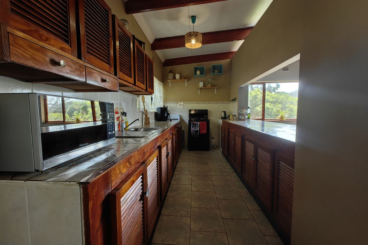 A galley-style kitchen featuring wooden cabinetry, tiled countertops, and exposed timber ceiling beams, offering a functional layout with natural light.