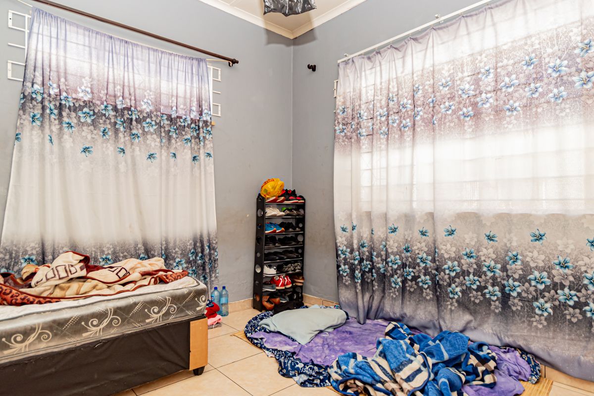 A bedroom featuring tiled flooring and windows fitted with security bars, requiring cosmetic updates to the wall finishes.