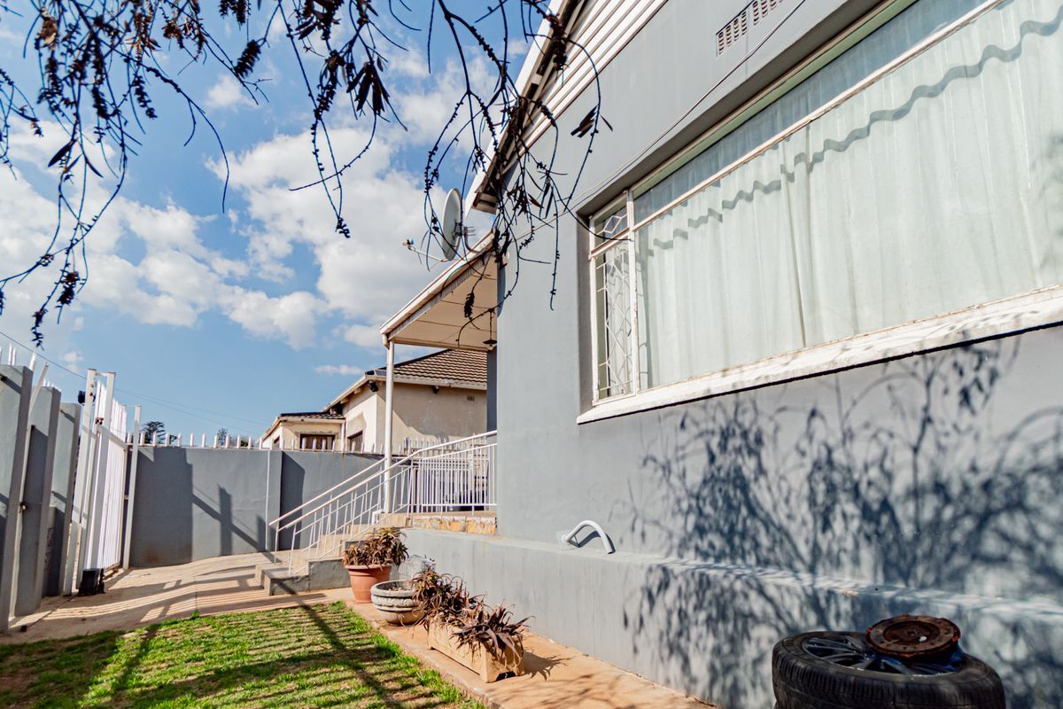 Rear exterior view of the property featuring a concrete patio area, security fencing, and metal staircase access to the building.