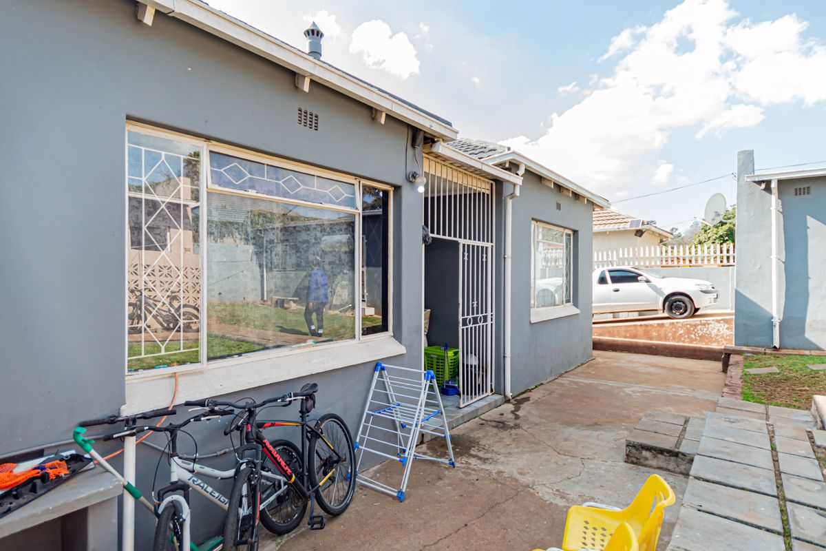 Rear exterior view of the house featuring concrete paving, security gate, and metal window frames.