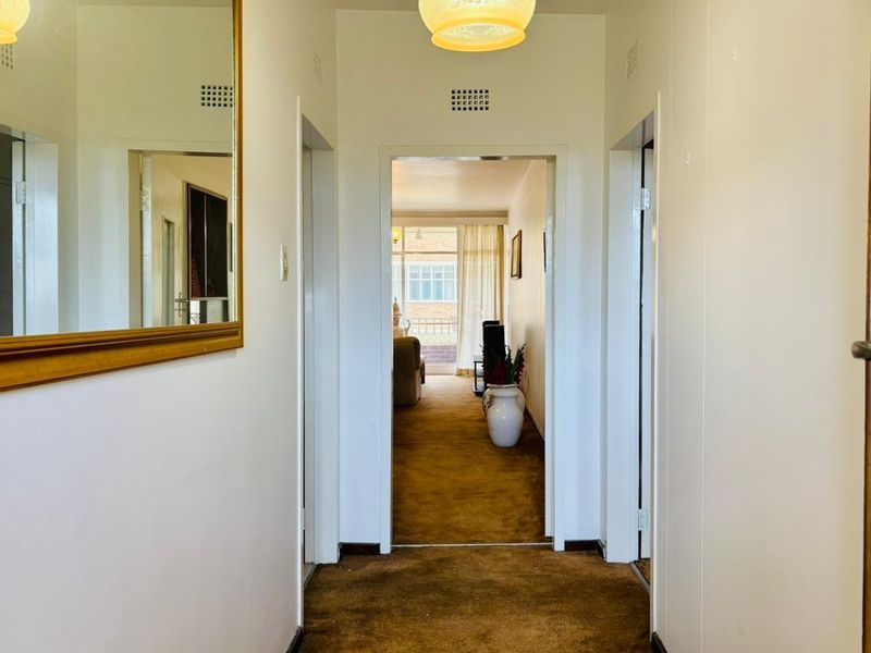 A central hallway featuring carpeted flooring, providing access to adjacent rooms and leading towards a bright living area with balcony access.