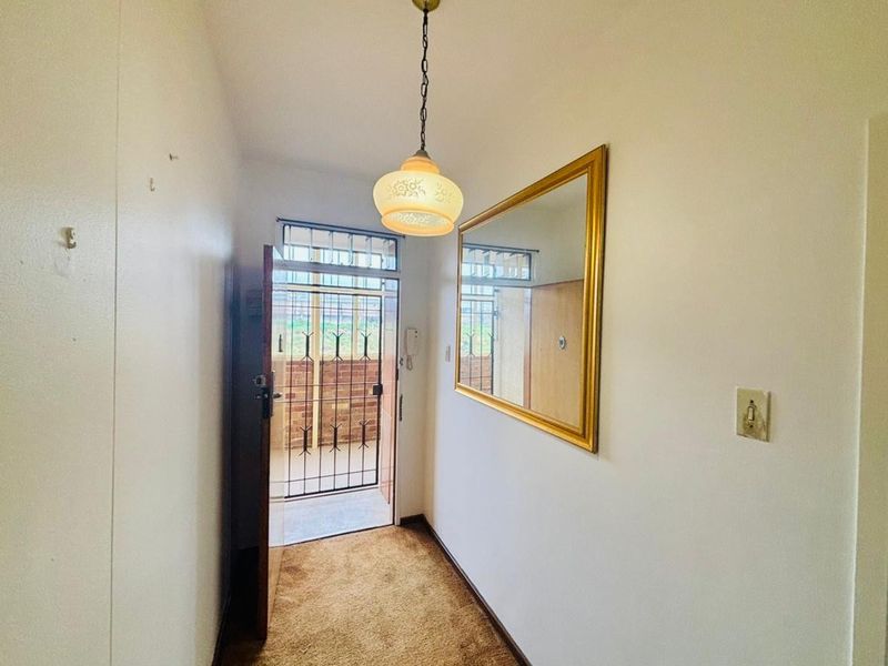 A functional entrance hallway featuring carpeted flooring, a wall-mounted mirror, and a security gate at the main entry point.