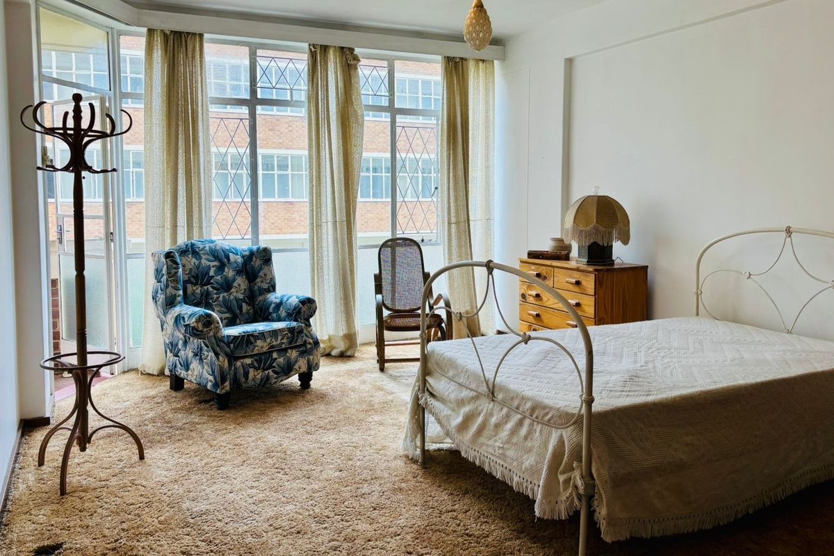 A spacious bedroom featuring large windows with access to a balcony, carpeted flooring, and neutral wall finishes.
