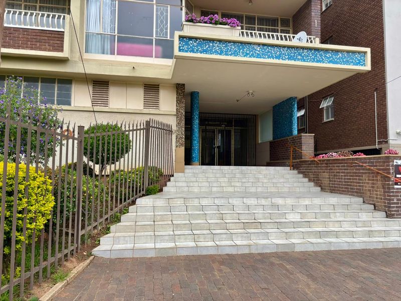 The front entrance of the apartment building features a wide tiled staircase leading to a covered lobby area with decorative blue mosaic accents.