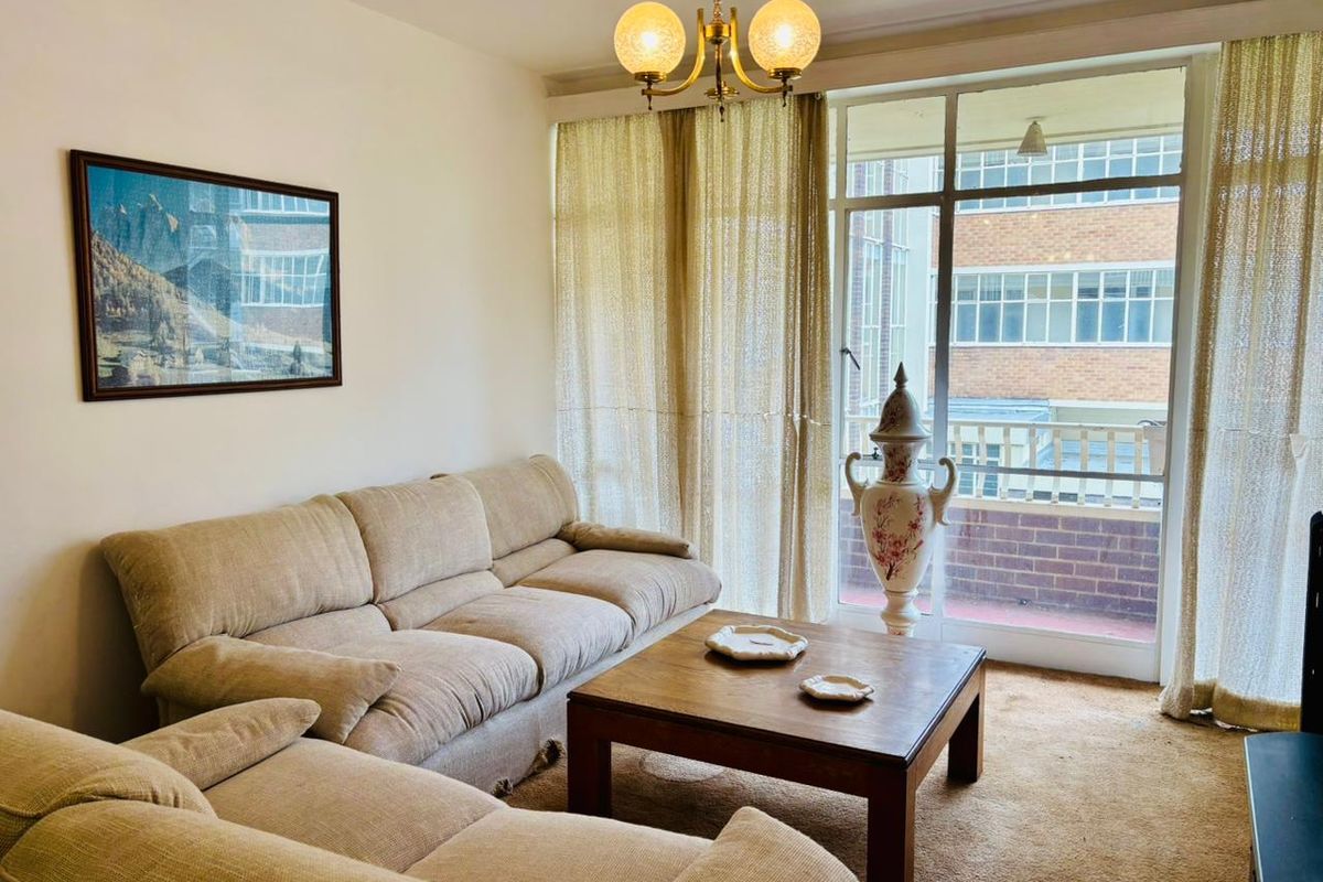 A living room featuring large windows with access to a balcony, providing natural light and a view of the surrounding building exterior.