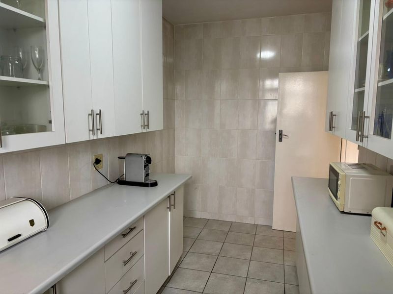 A functional kitchen featuring white cabinetry, neutral countertops, and tiled flooring, providing a clean and practical workspace.