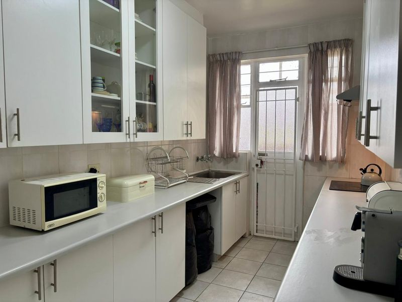 Functional galley-style kitchen featuring white cabinetry, tiled splashbacks, stainless steel sink, and direct access to an exterior door.