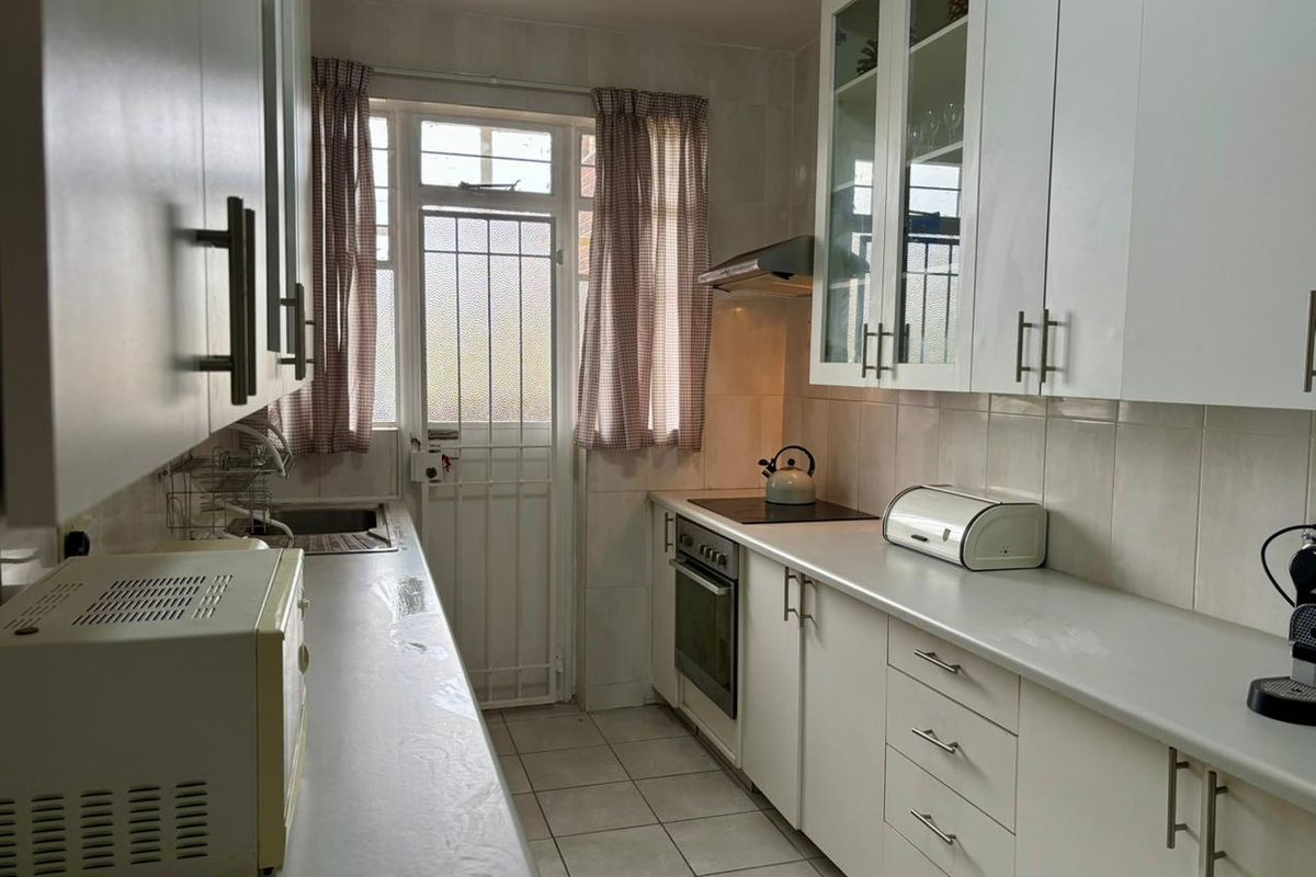 A functional galley-style kitchen featuring white cabinetry, integrated oven and hob, extractor fan, and direct access to an exterior door.