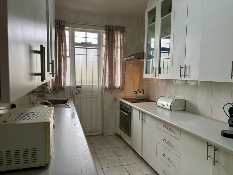 A functional galley-style kitchen featuring white cabinetry, integrated oven and hob, extractor fan, and direct access to an exterior door.