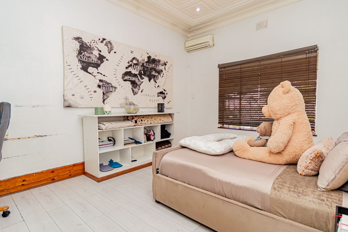 A bedroom featuring a pressed metal ceiling, air conditioning unit, and laminate flooring, currently showing signs of wear on the walls and skirting boards.