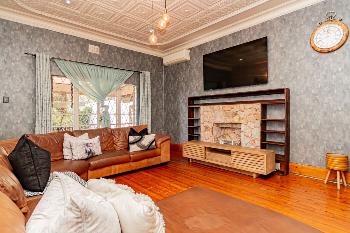 Spacious living room featuring a decorative pressed metal ceiling, stone fireplace with built-in shelving, and polished timber flooring.