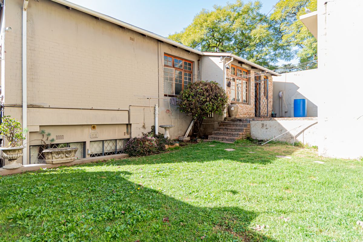Rear view of the property featuring a brick facade, timber-framed windows, and a private lawn area with external access stairs.