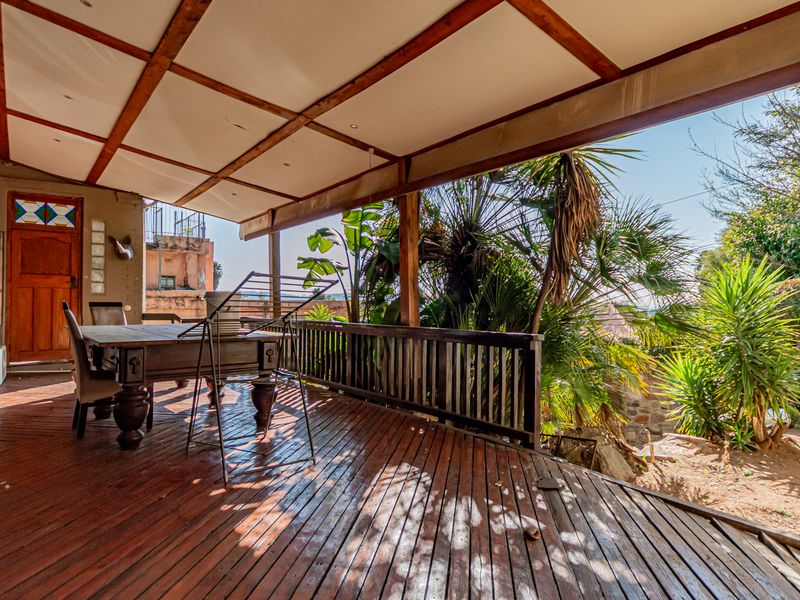 A spacious covered timber deck patio featuring exposed beams and a timber balustrade, overlooking a landscaped garden area.