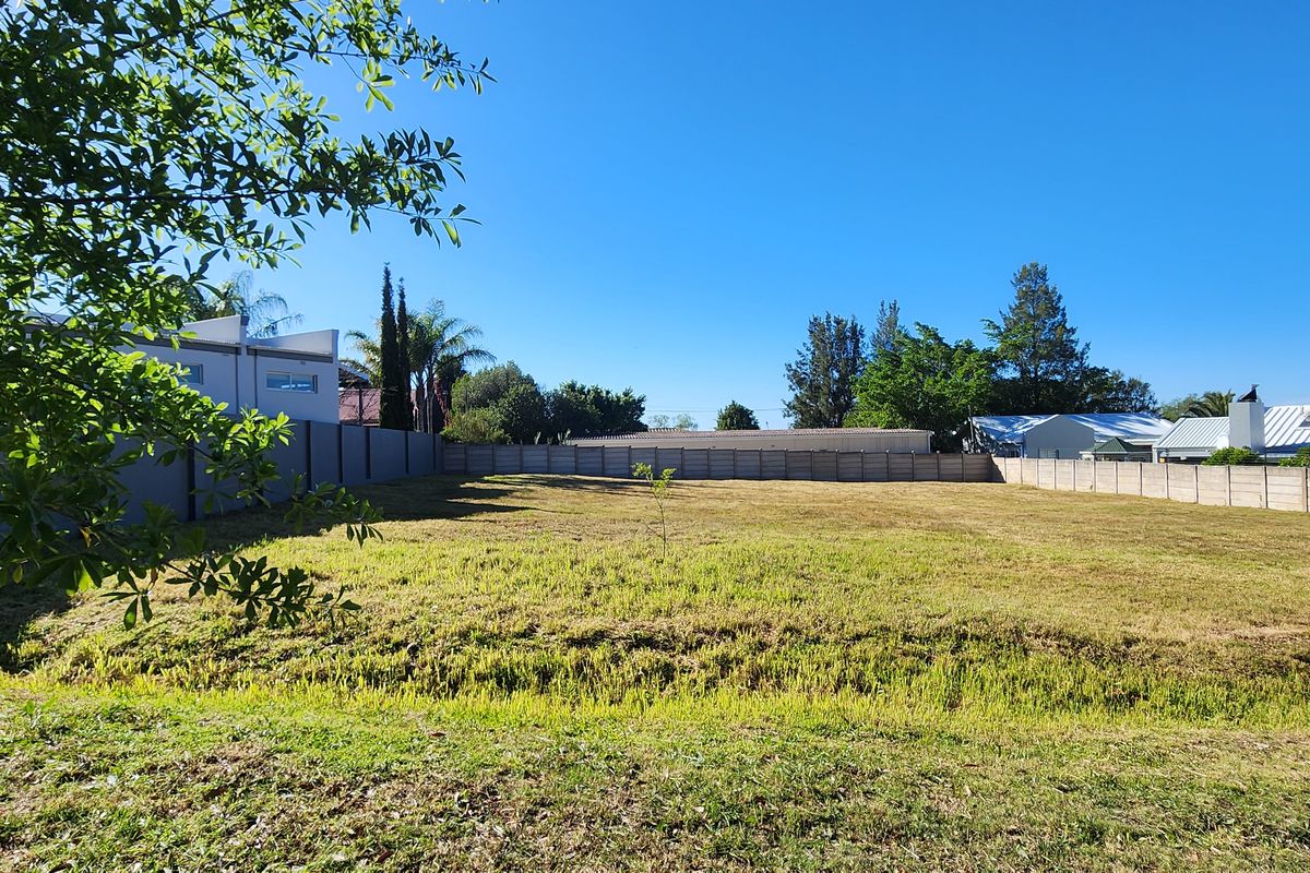 A vacant residential plot featuring a level grass lawn enclosed by perimeter boundary walls in a established neighborhood setting.