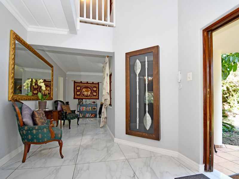 A bright and welcoming entrance hall featuring polished marble-look floor tiles, a high ceiling, and a staircase leading to the upper level.