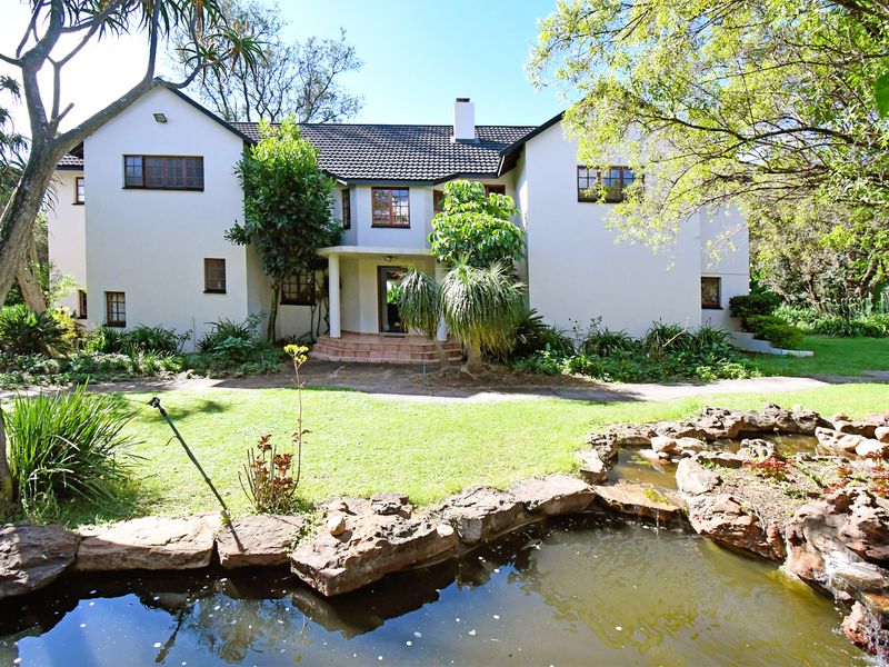 A well-maintained rear elevation of a two-story house featuring a landscaped garden, stone-lined pond, and paved pathway leading to the entrance.