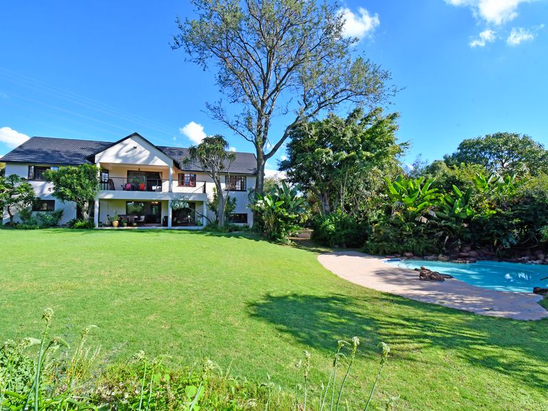 Spacious rear exterior view featuring a large manicured lawn, a swimming pool with rock features, and a two-story house with a balcony and patio.