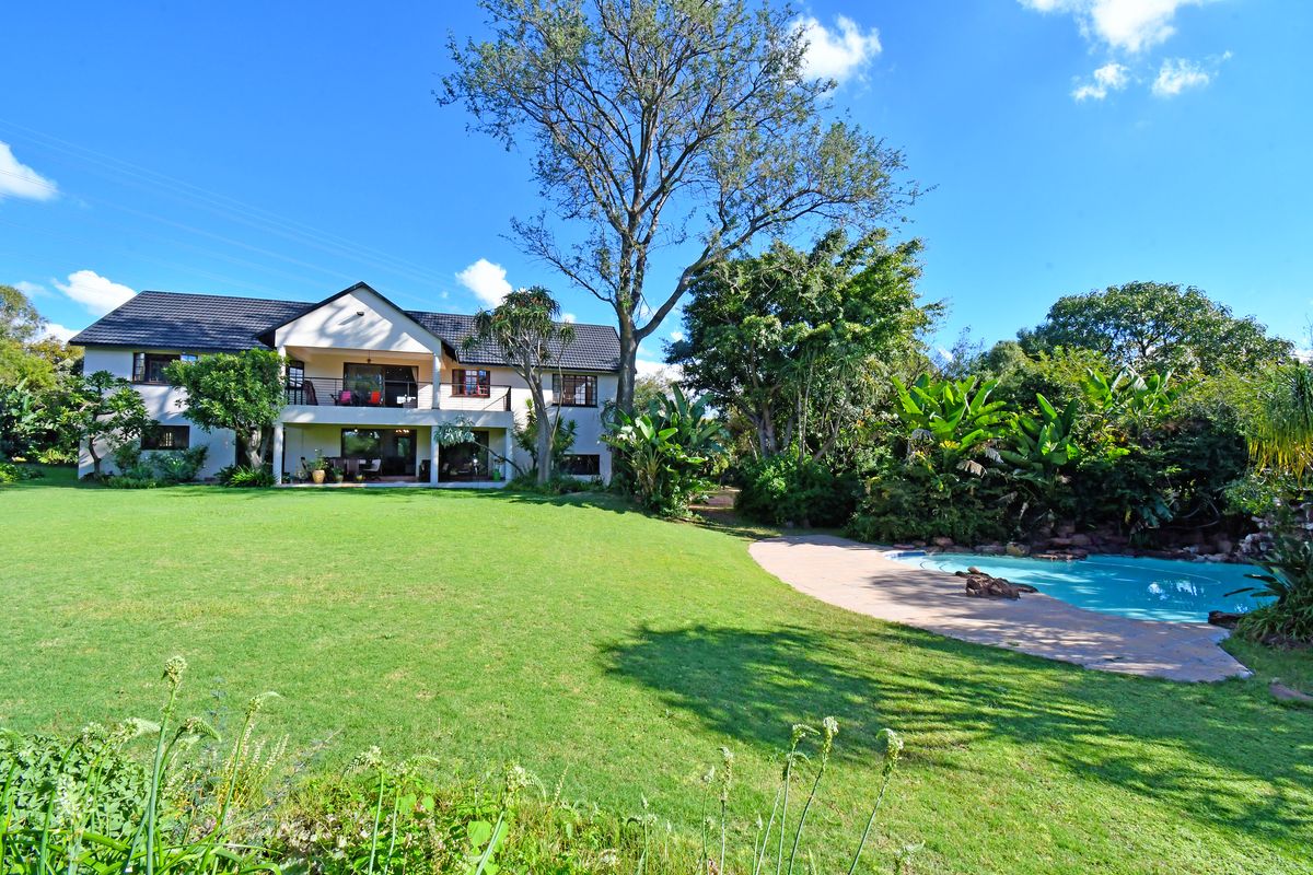 Spacious rear exterior view featuring a large manicured lawn, a swimming pool with rock features, and a two-story house with a balcony and patio.