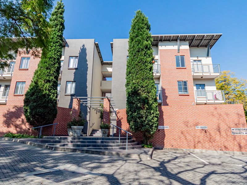 Front elevation of a modern brick apartment complex featuring paved driveway access, balconies, and landscaped entrance area.