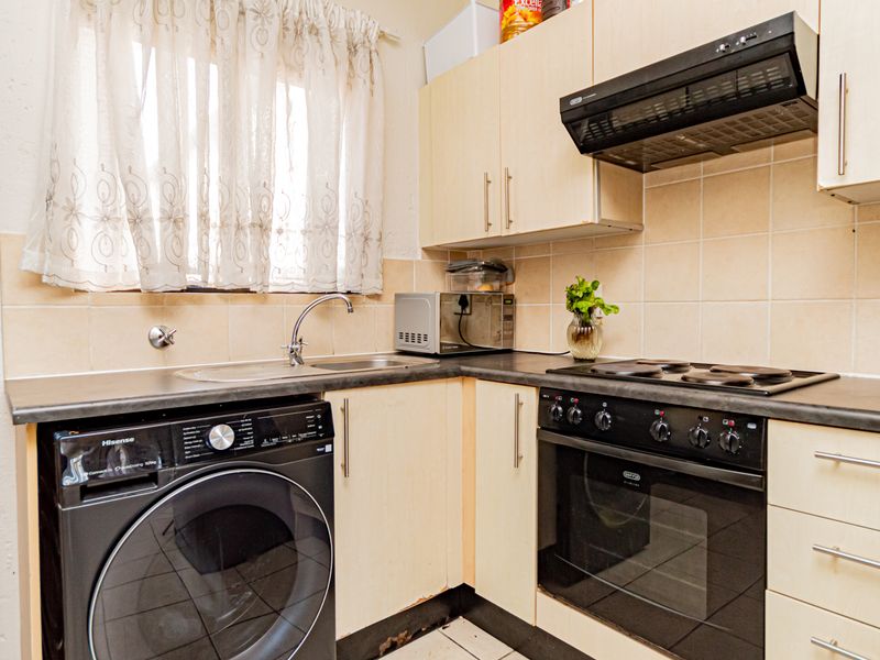 Compact kitchen featuring laminate cabinetry, tiled backsplash, built-in oven with hob, and integrated laundry plumbing, showing signs of wear on base cabinetry.