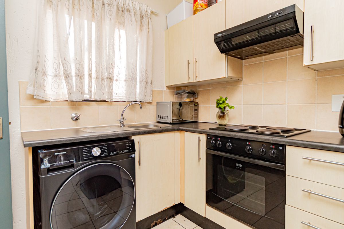 Compact kitchen featuring laminate cabinetry, tiled backsplash, built-in oven with hob, and integrated laundry plumbing, showing signs of wear on base cabinetry.