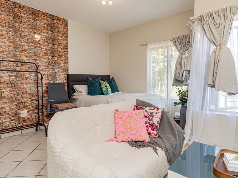 A bedroom featuring a textured stone-effect feature wall, tiled flooring, and large windows allowing for natural light.