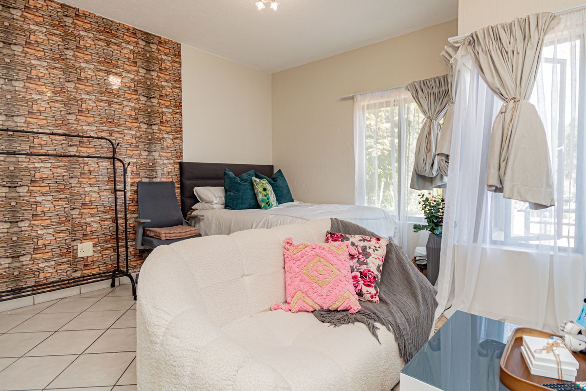 A bedroom featuring a textured stone-effect feature wall, tiled flooring, and large windows allowing for natural light.