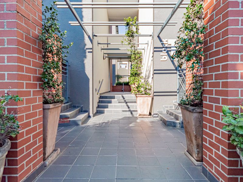 A well-maintained apartment complex entrance featuring brick pillars, a tiled walkway, and a modern metal pergola structure.