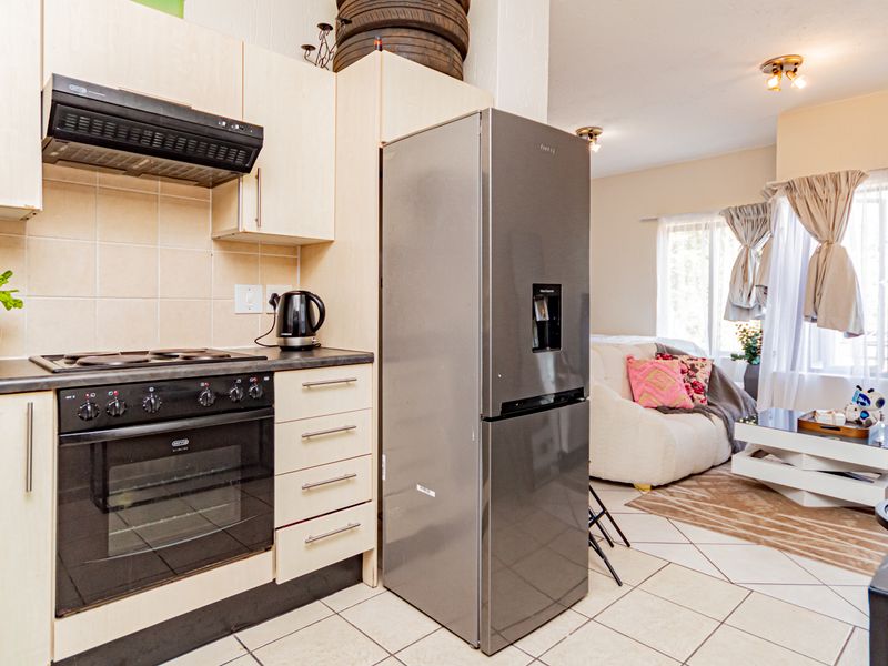 Open-plan kitchen and living area featuring light-toned cabinetry, built-in oven, electric hob, and tiled flooring throughout the space.