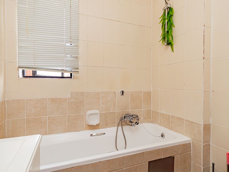A dated bathroom featuring a standard bathtub with shower mixer, ceramic wall tiling, and a toilet, requiring cosmetic updates to improve its overall condition.