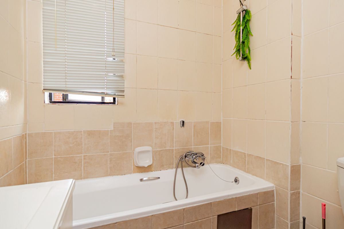A dated bathroom featuring a standard bathtub with shower mixer, ceramic wall tiling, and a toilet, requiring cosmetic updates to improve its overall condition.