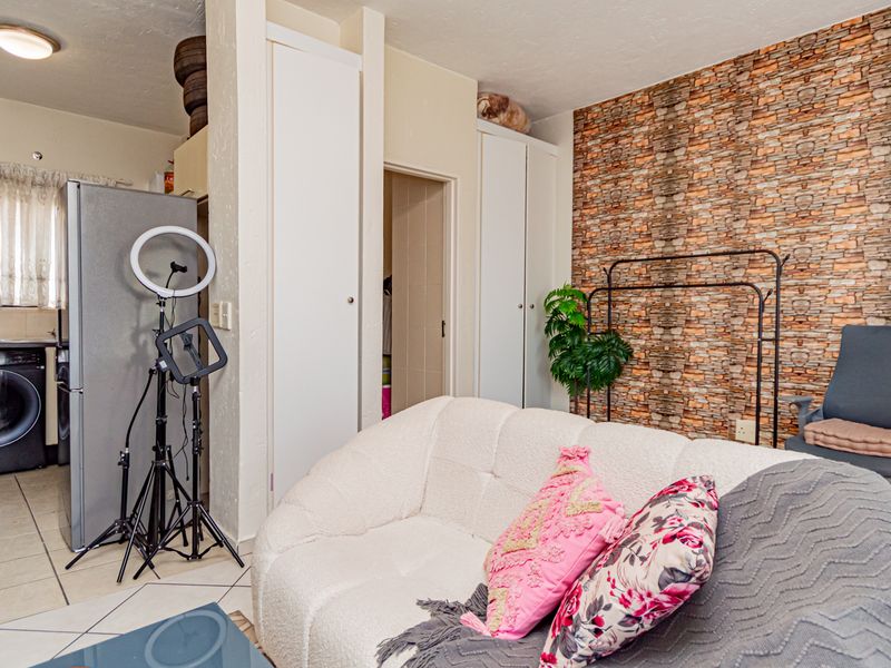 Open-plan living area featuring tiled floors, built-in storage cupboards, and a decorative brick-effect feature wall, with an integrated laundry space.