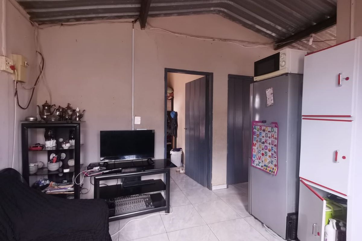 A living area featuring tiled flooring and an exposed corrugated metal roof, requiring cosmetic updates to improve the overall finish and aesthetic appeal.