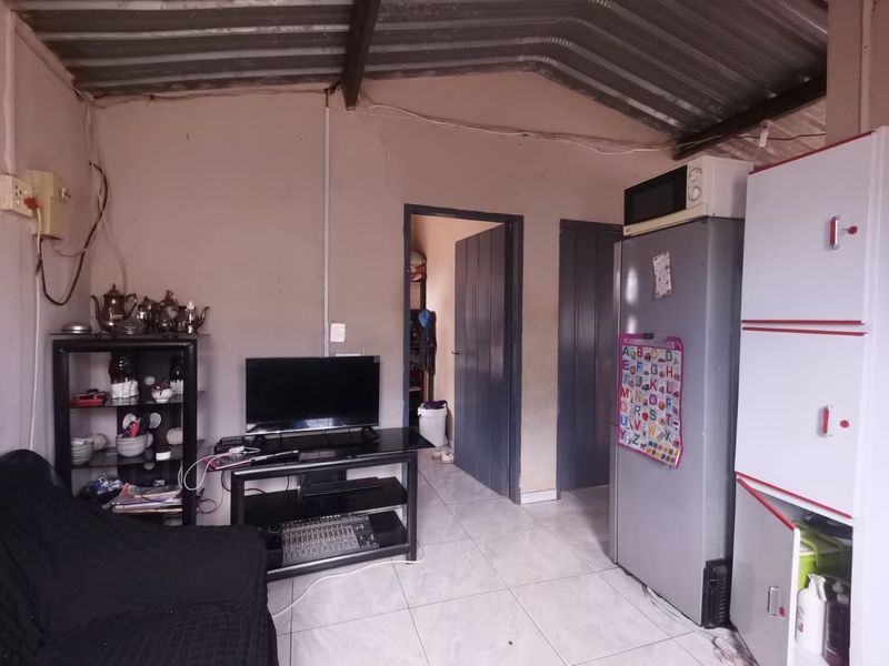 A living area featuring tiled flooring and an exposed corrugated metal roof, requiring cosmetic updates to improve the overall finish and aesthetic appeal.