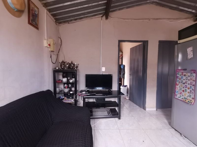 A living area featuring tiled flooring and an exposed roof structure, requiring cosmetic updates and finishing to improve the overall aesthetic and condition.