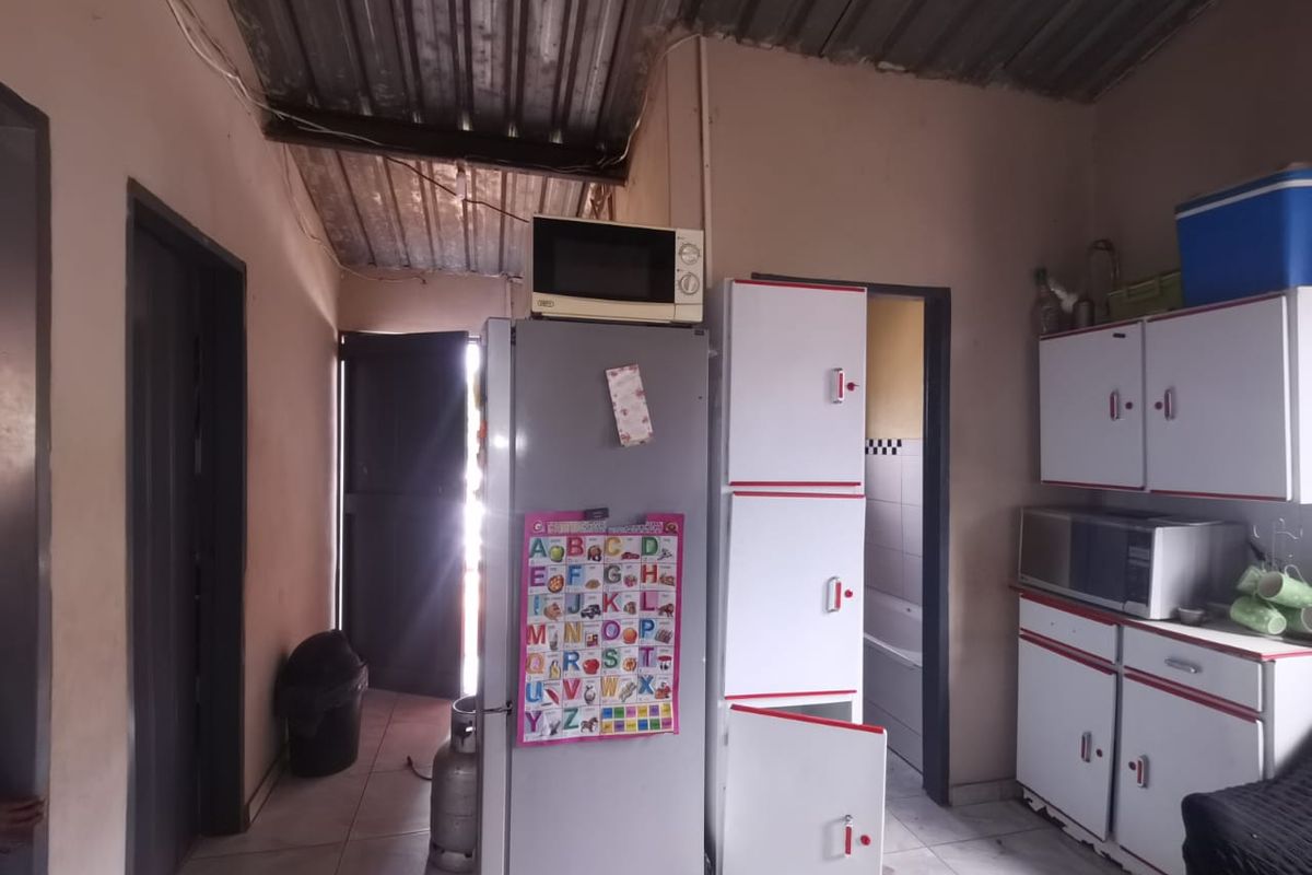 A functional kitchen area featuring built-in cabinetry, tiled flooring, and a corrugated metal ceiling, requiring cosmetic updates to improve its overall condition.