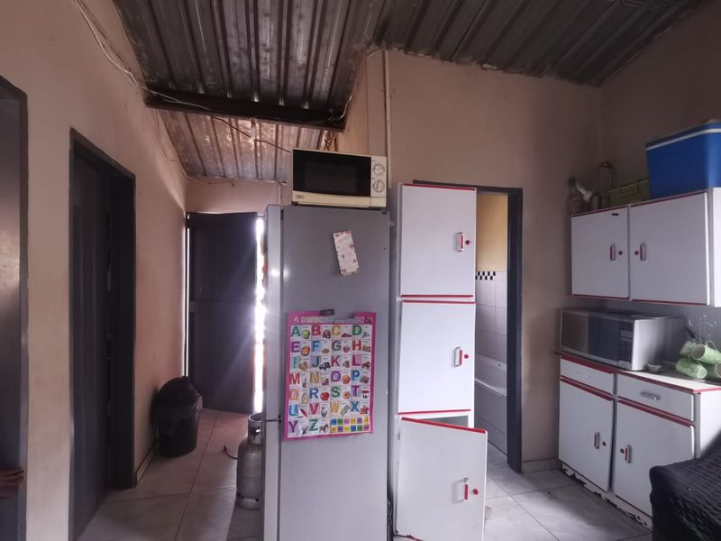 A functional kitchen area featuring built-in cabinetry, tiled flooring, and a corrugated metal ceiling, requiring cosmetic updates to improve its overall condition.