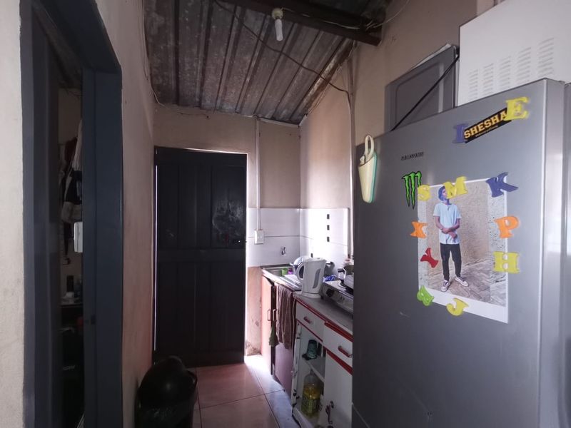 A compact scullery area featuring basic built-in cabinetry, a sink, and a corrugated metal ceiling, requiring cosmetic updates to improve functionality and aesthetic appeal.