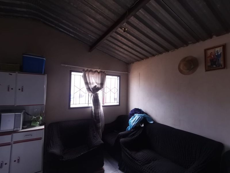 A living area featuring a corrugated metal ceiling and a window fitted with security bars.