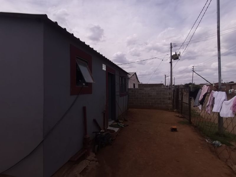 Rear exterior view of the property featuring a corrugated metal roof, concrete block boundary wall, and metal security gate.