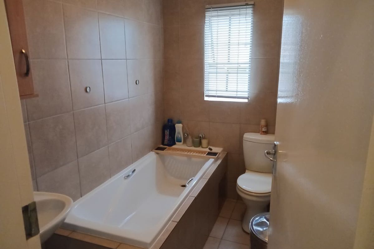 A functional bathroom featuring a built-in bathtub, toilet, and neutral wall tiling with a window for natural light.