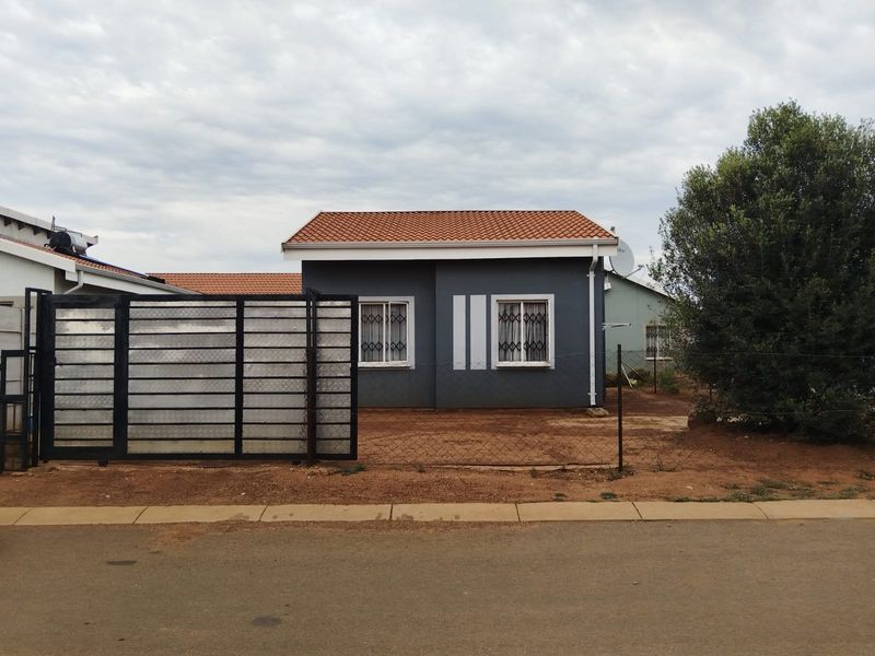 Front elevation of a detached house featuring a tiled roof, security bars on windows, and a gated entrance with an unpaved yard area.