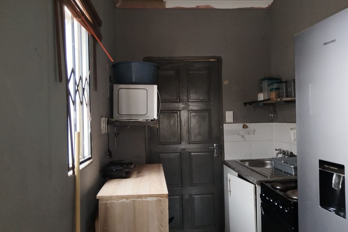 A compact kitchen area featuring a stainless steel sink, tiled splashback, and built-in cabinetry, currently requiring cosmetic updates and ceiling finishing.