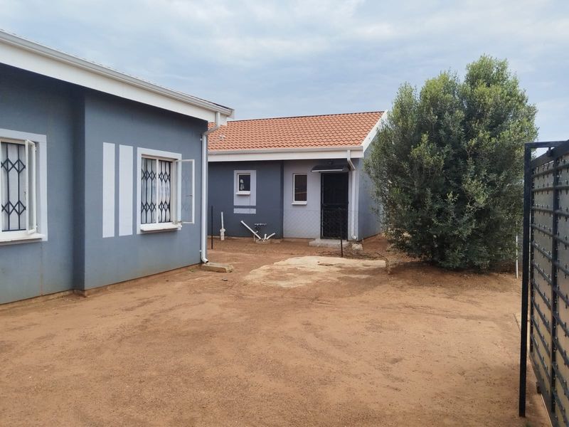 Rear view of the property showing the exterior walls, tiled roof, and unpaved yard area with security features on windows and doors.