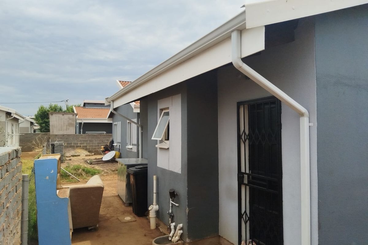 Rear exterior view of the property showing the side facade, security gate, and external plumbing infrastructure.