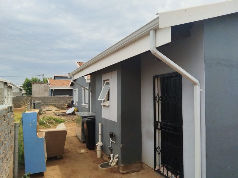Rear exterior view of the property showing the side facade, security gate, and external plumbing infrastructure.
