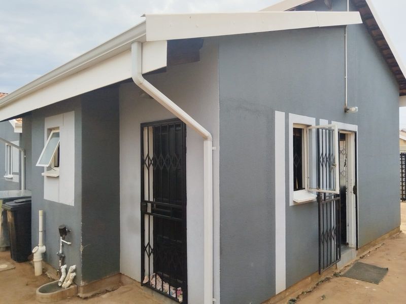 Rear exterior view of the house featuring grey painted walls, white trim, security gates, and functional external plumbing and gutter systems.